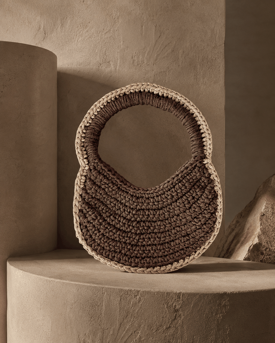 Bolsa Olhos da Terra · peça marrom escultural sobre pedestal terracota · TUÁ